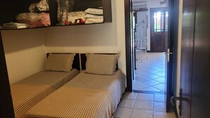 A room with two beds, a shelf with various items, and a view of the hallway and outside. - House located 200 m from the beach, leisure area, restaurants, bars and shops (Mata de São João)