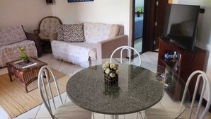 A living room with a round glass table, two sofas, a coffee table, and a TV. - House located 200 m from the beach, leisure area, restaurants, bars and shops (Mata de São João)