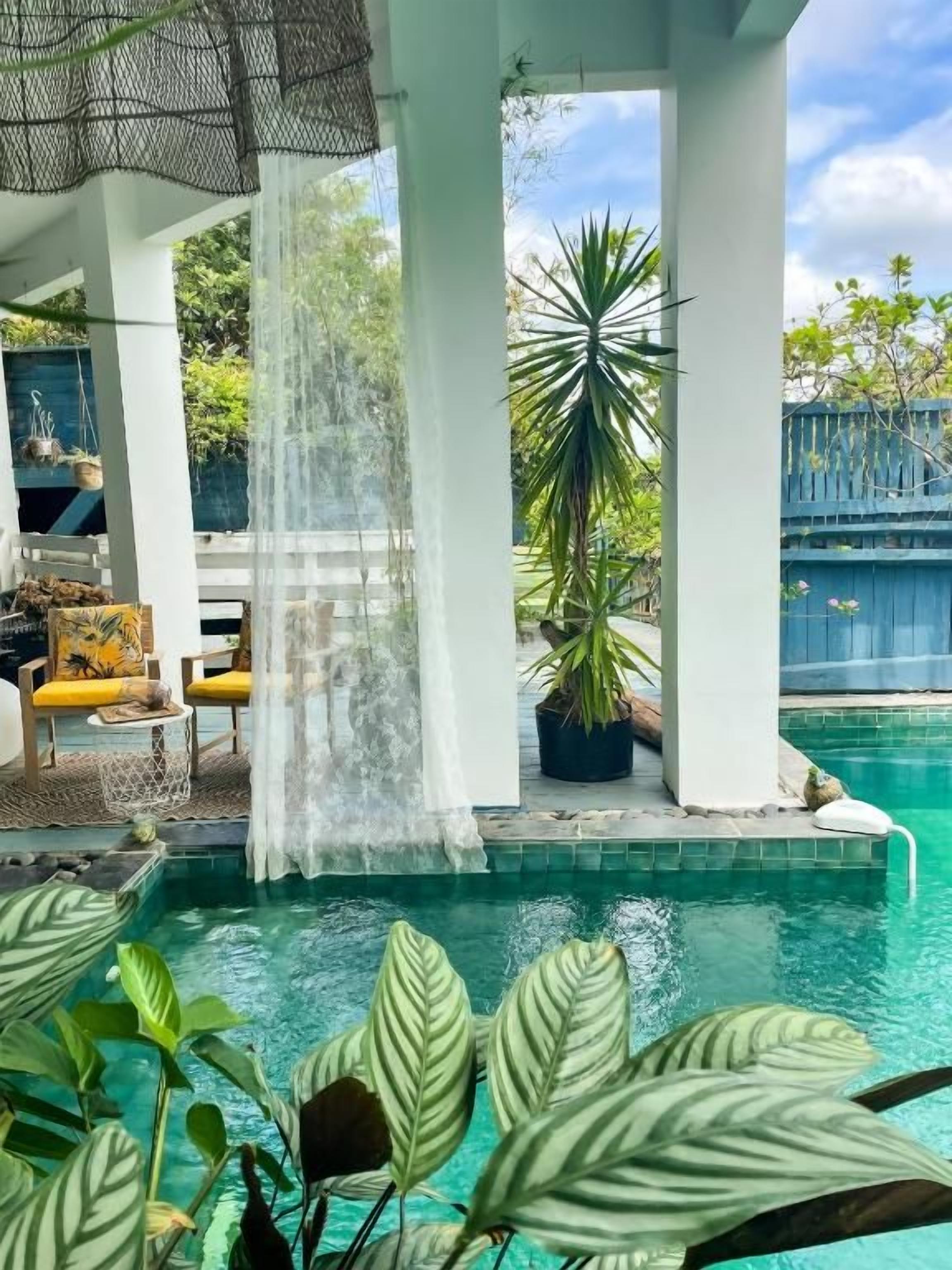 A pool area with a waterfall feature, surrounded by potted plants and a covered seating area.