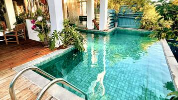 A swimming pool with a wooden deck and potted plants.