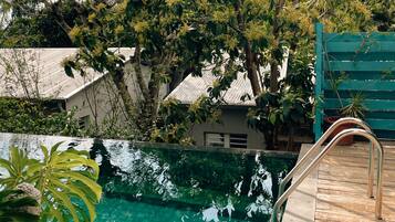 A swimming pool with a wooden deck, surrounded by lush greenery and trees.