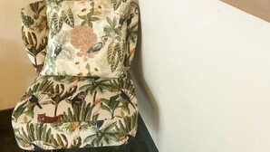 A chair with a tropical leaf pattern, a vase with flowers, and a wall with a leaf pattern. - Le Jardin De Ravintsara - Adults Only (Saint-Pierre)