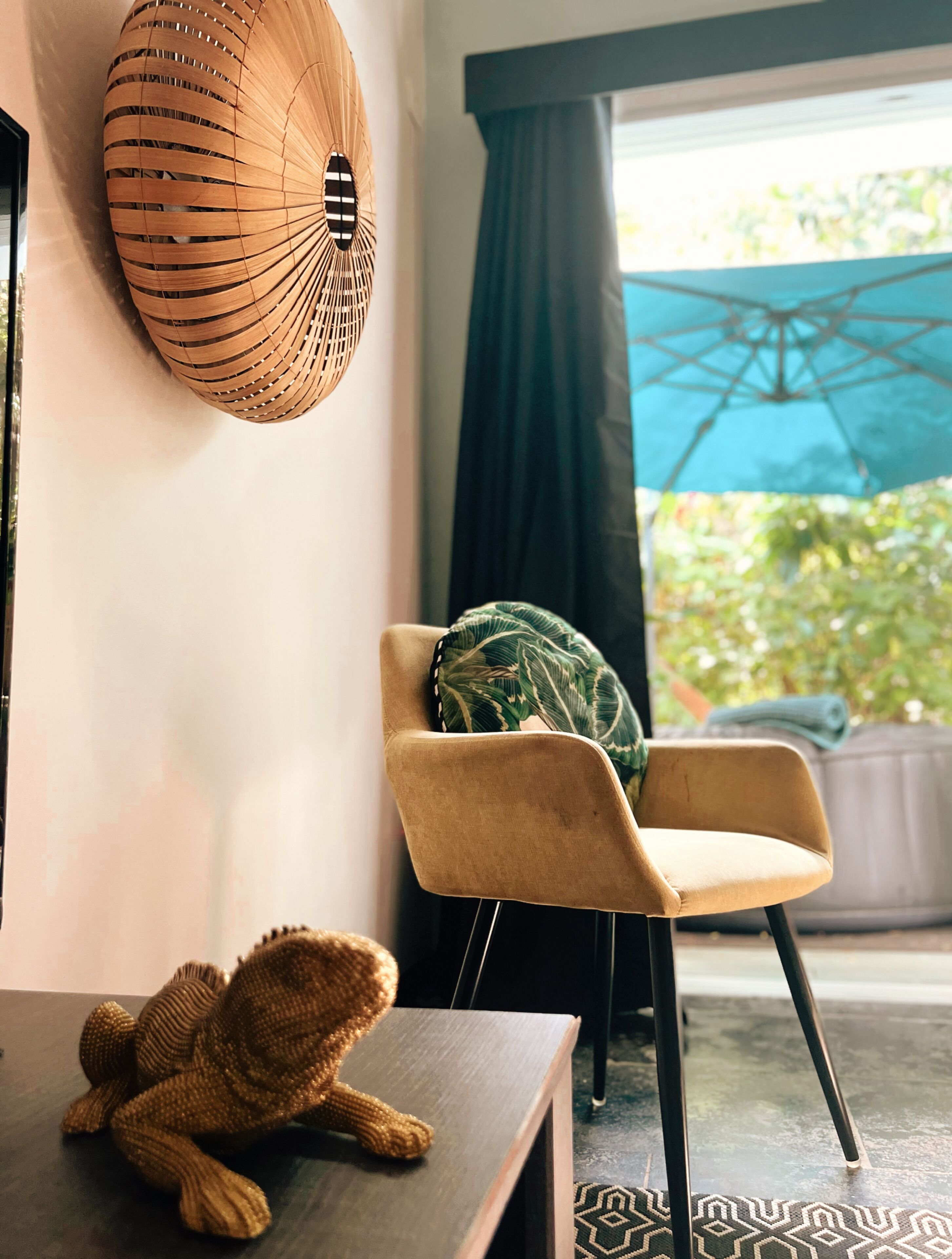 A room with a woven wall hanging, a chair with a green cushion, and a small knitted animal on a table.
