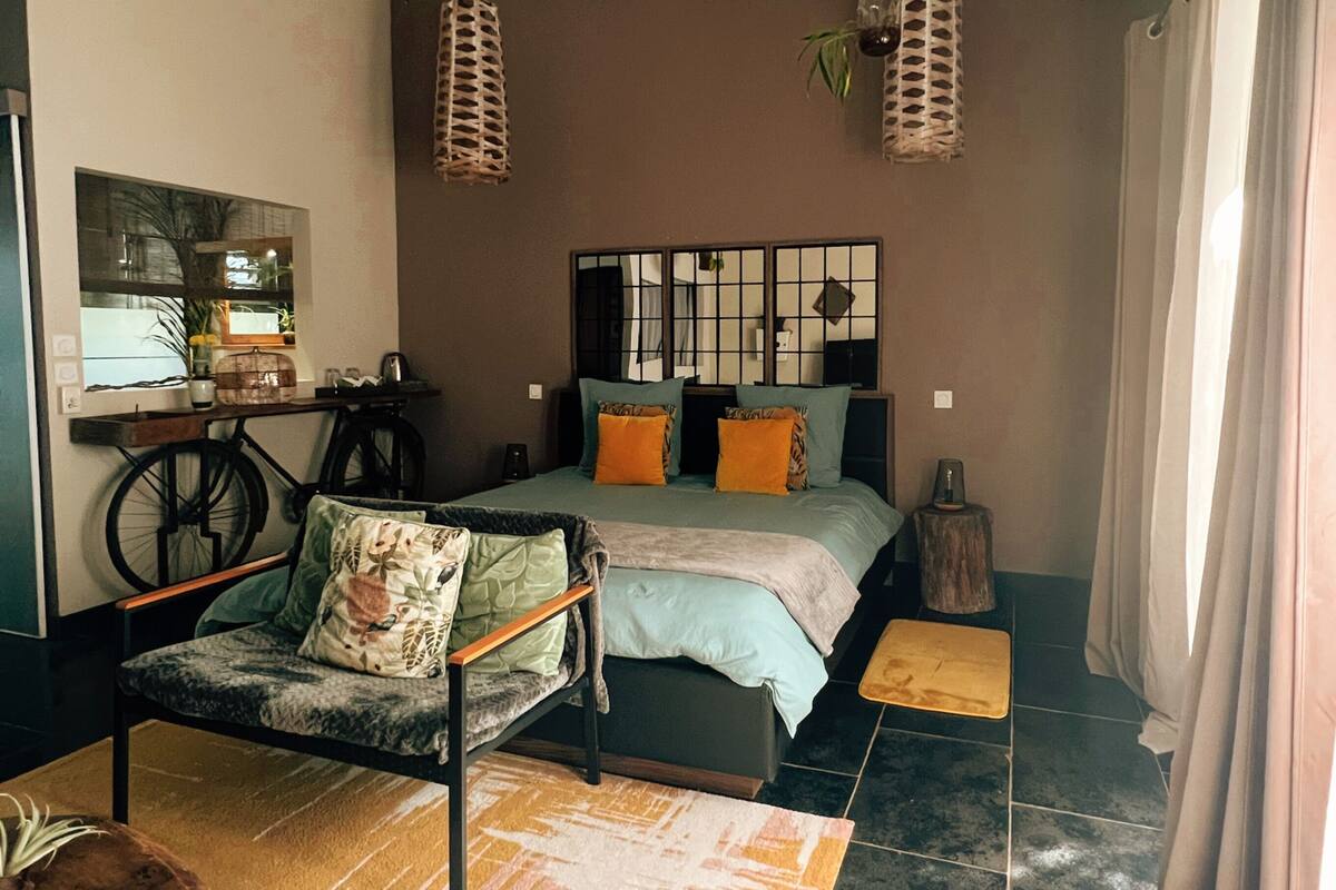 A bedroom with a bed, a chair, a small table, a mirror, and hanging lights.