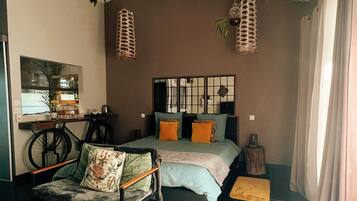 A bedroom with a bed, a chair, a small table, a mirror, and hanging lights.