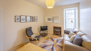 A living room with a sofa, a chair, a TV, a fireplace, and framed pictures on the wall. - Cozy Apartment near The Meadows (Edinburgh)