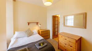 A bedroom with a bed, bedside table, dresser, and a mirror on the wall. - Cozy Apartment near The Meadows (Edinburgh)