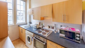 A compact kitchen with wooden cabinets, a washing machine, a microwave, and a toaster. - Cozy Apartment near The Meadows (Edinburgh)