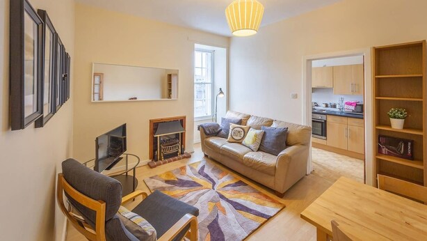A modern living room with a sofa, a television, a fireplace, and a dining area. - Cozy Apartment near The Meadows (Edinburgh)
