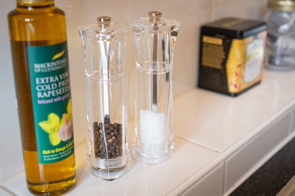 A kitchen counter with a bottle of extra virgin cold press rapeseed oil, two glass containers with spices, and a box of tea.