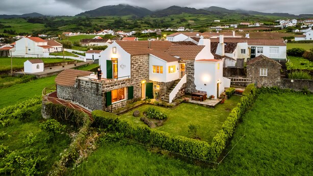Un village rural aux maisons en pierre, doté d’un jardin bien entretenu et offrant une vue sur des collines verdoyantes à l’horizon.