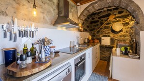 Une cuisine aux murs en pierre, avec un plafond en bois et un four encastré.