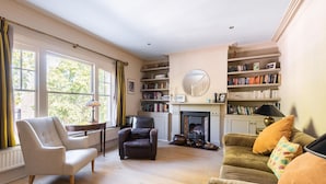 Uma sala de estar ampla, com lareira, estantes de livros e assentos confortáveis.