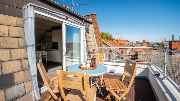 Terraço no telhado com mesa e cadeiras, porta de correr de vidro que dá para uma cozinha, e vista para a paisagem urbana.