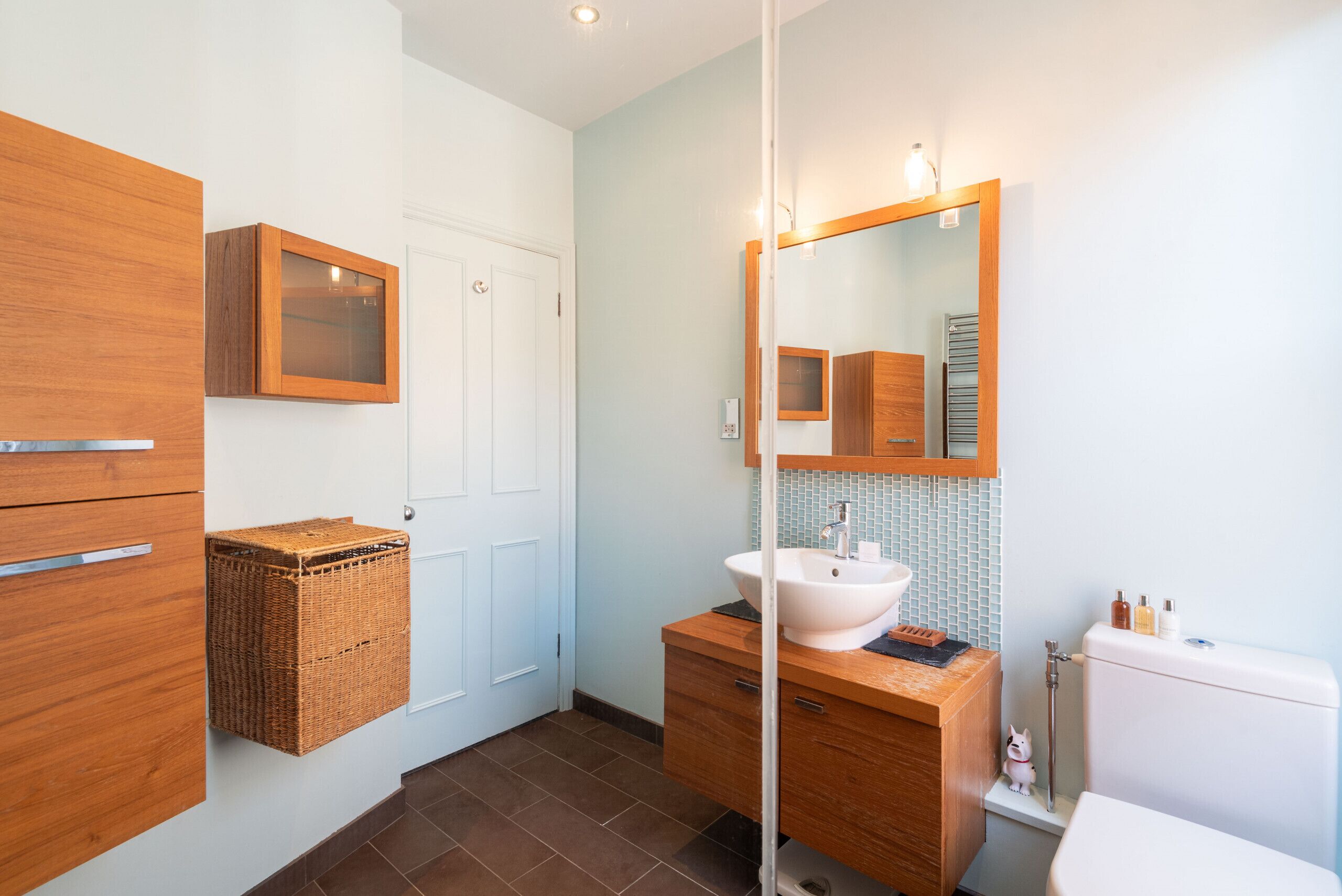 A bathroom with a wooden vanity, a white sink, a mirror, and a small basket.