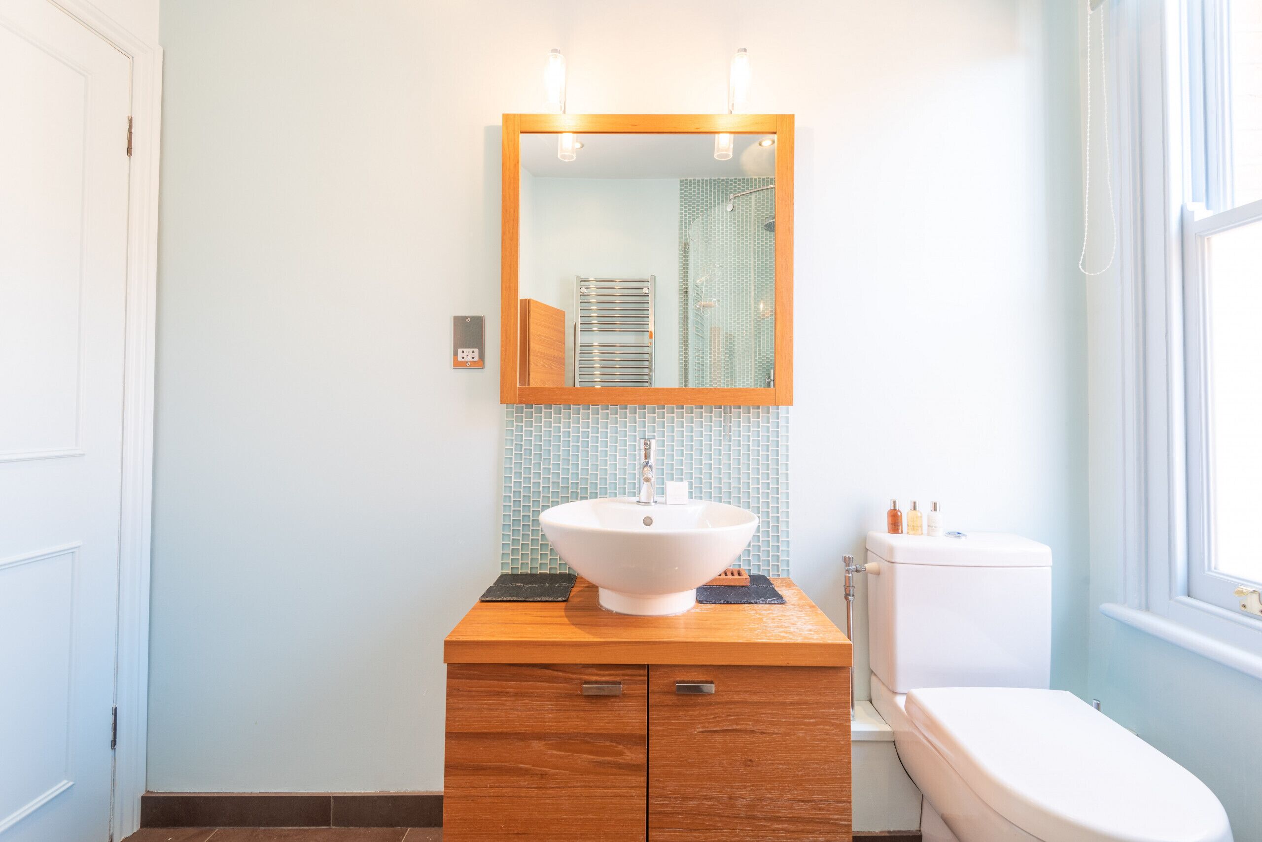A bathroom with a wooden vanity, a white sink, a mirror, and a toilet.