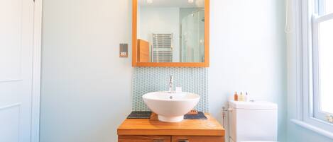 A bathroom with a wooden vanity, a white sink, a mirror, and a toilet.