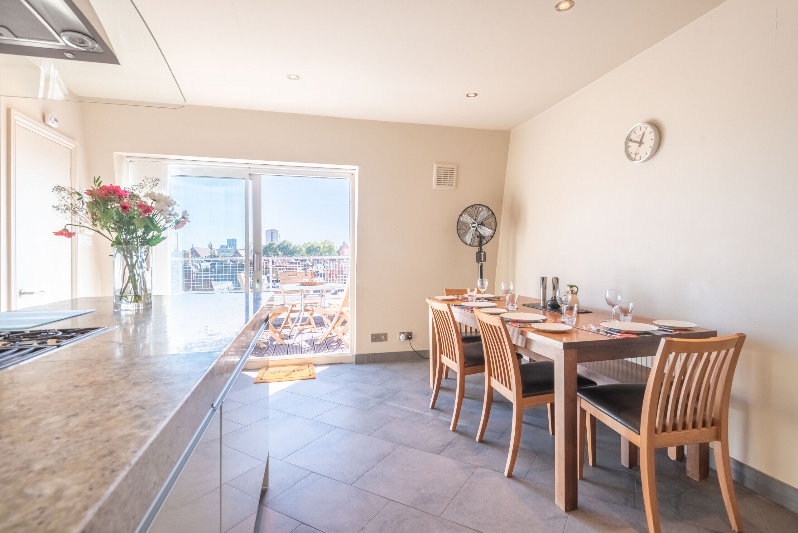 A modern kitchen with a large window, a dining area with wooden chairs, and a view of the city.