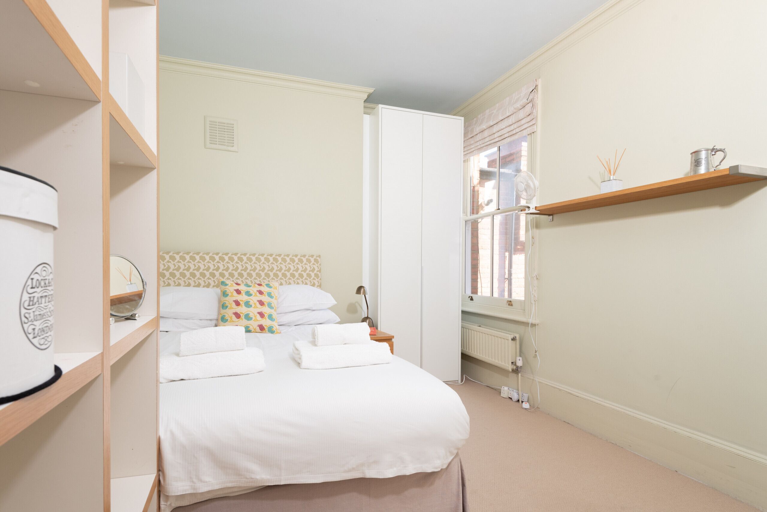 A neatly arranged bedroom with a bed, bedside table, and a shelf with a lamp.