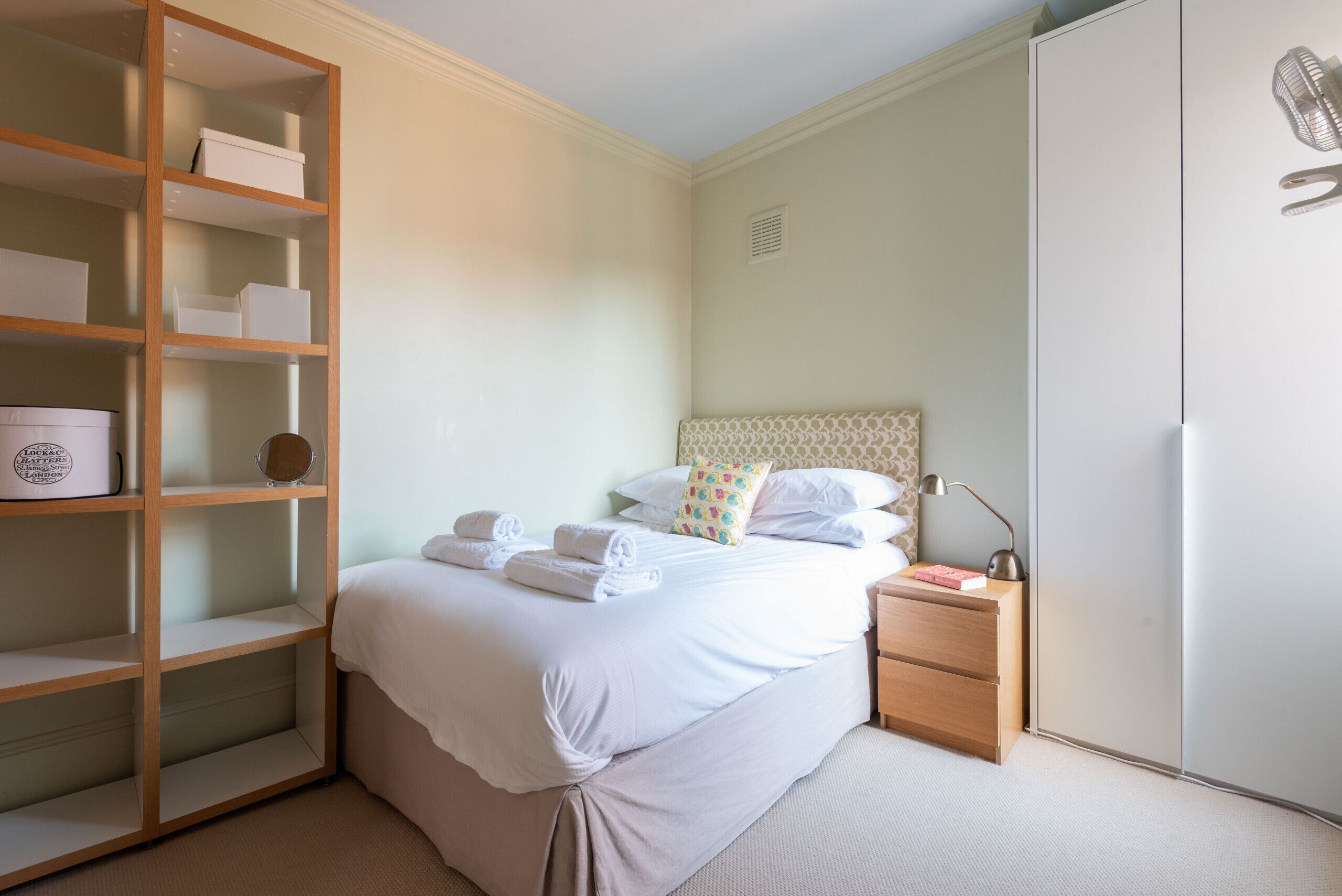 Une chambre bien rangée, avec un lit, une table de chevet et une bibliothèque intégrée.