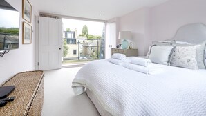 A bedroom with a large bed, a bedside table with a lamp, and a view of buildings through an open door. - A Home on Northcote (London)