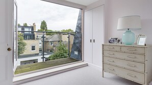 A room with a large window, a white dresser with drawers, and a teal lamp. - A Home on Northcote (London)