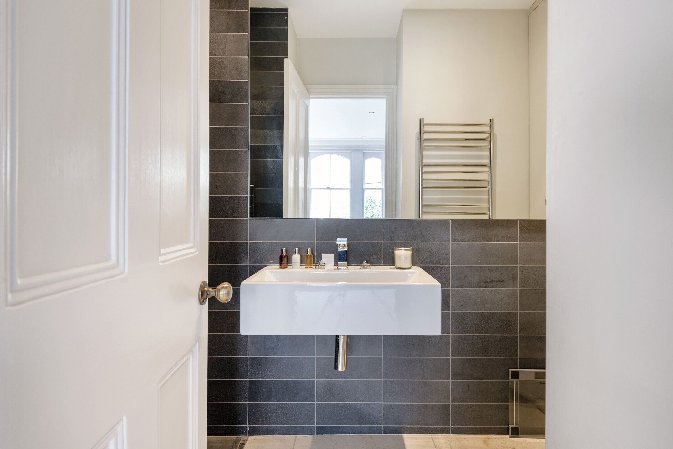 Een badkamer met een wit wastafel, donkere tegels, een spiegel en een handdoekhouder.