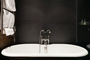 Ein modernes Badezimmer mit freistehender Badewanne, dunkel geflieste Wände und einem Handtuchhalter mit gefalteten Handtüchern.