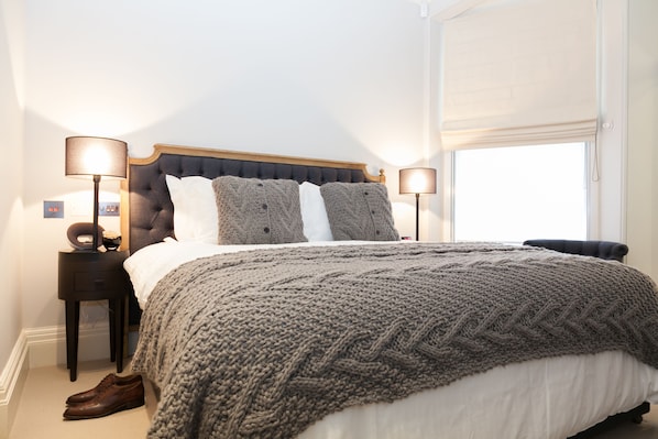 A neatly made bed with a grey knitted blanket, a wooden headboard, and two bedside lamps.