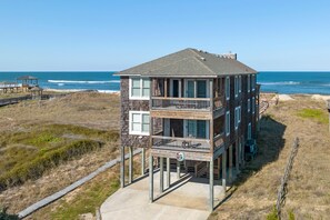 Une maison à deux étages située en bord de mer, dotée d’un balcon et d’une terrasse, offrant une vue sur l’océan.