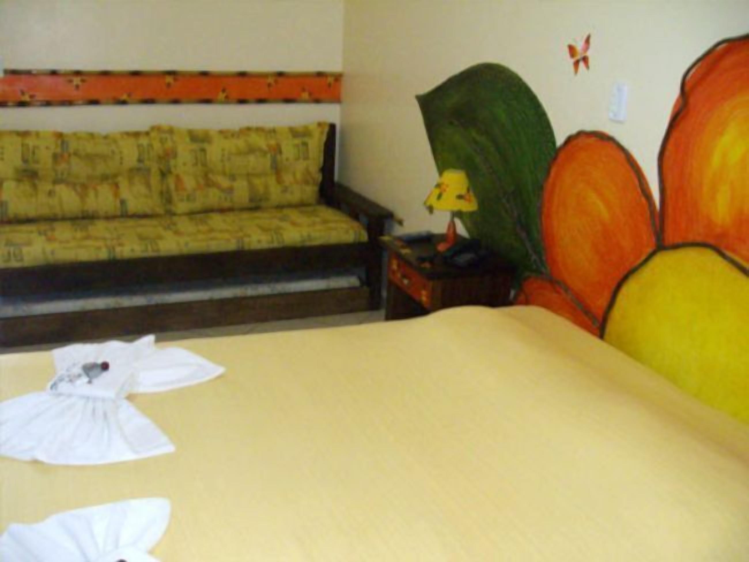 A hotel room with a bed, a sofa, a nightstand, and a wall with a large flower painting.