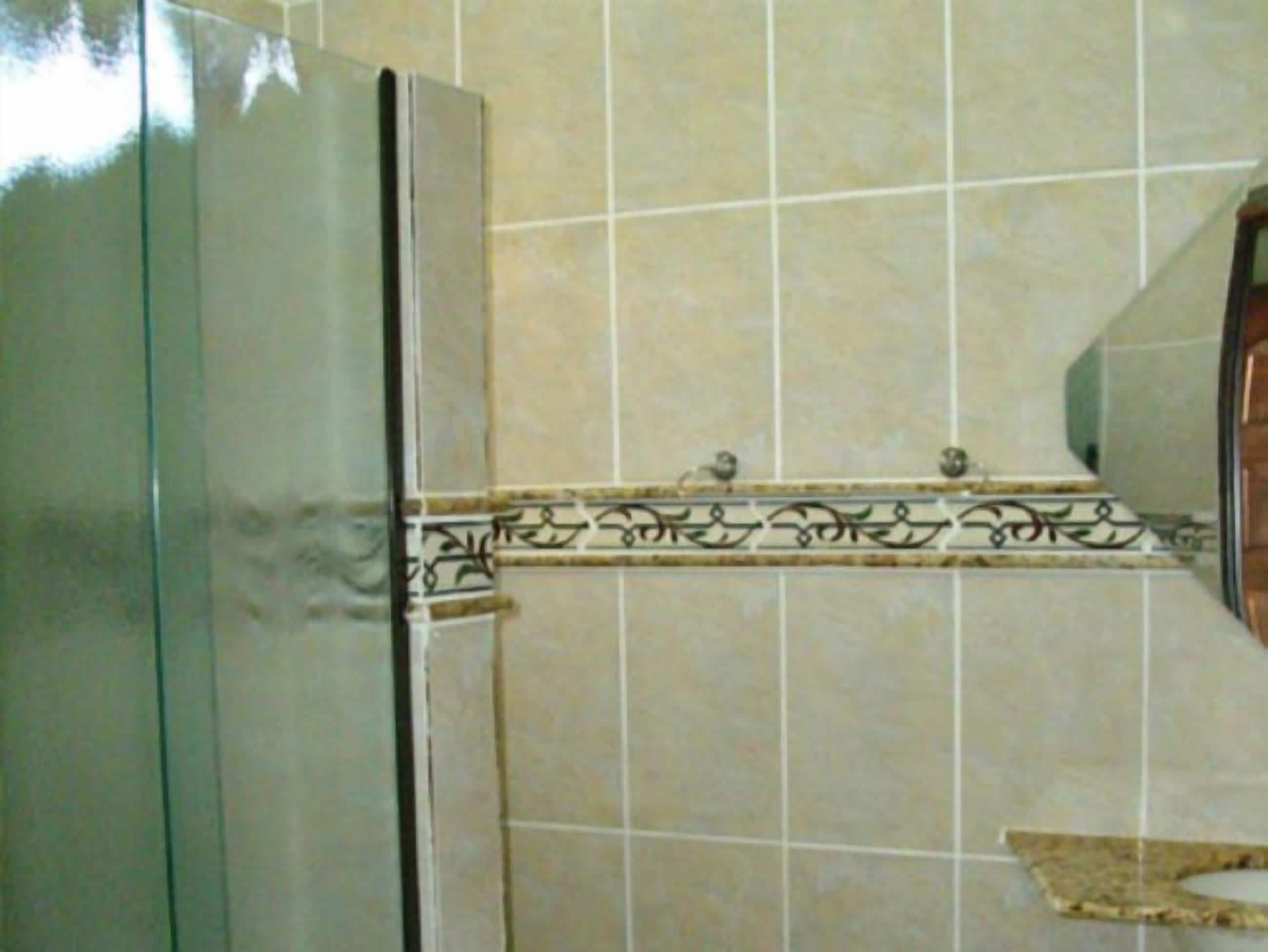 A bathroom with a tiled wall, a sink, and a mirror.