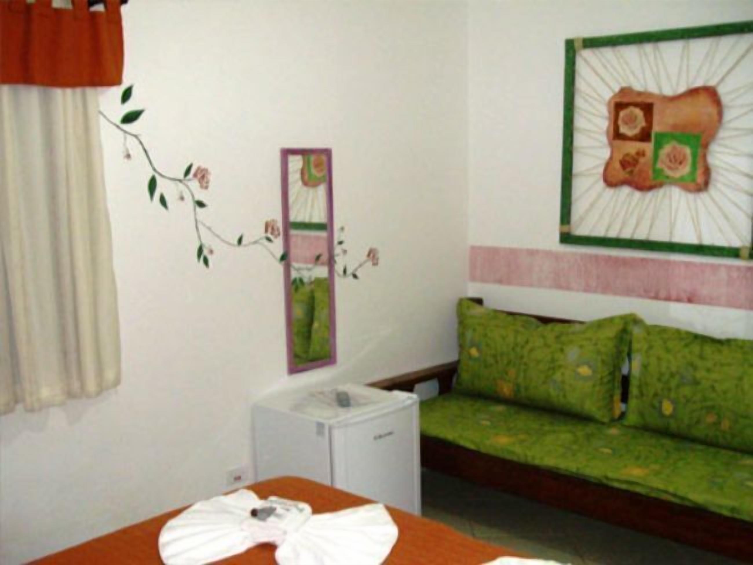 A bedroom with a bed, a green sofa, a small white cabinet, and a wall decoration.