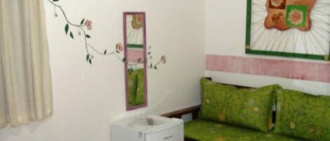 A bedroom with a bed, a green sofa, a small white cabinet, and a wall decoration.