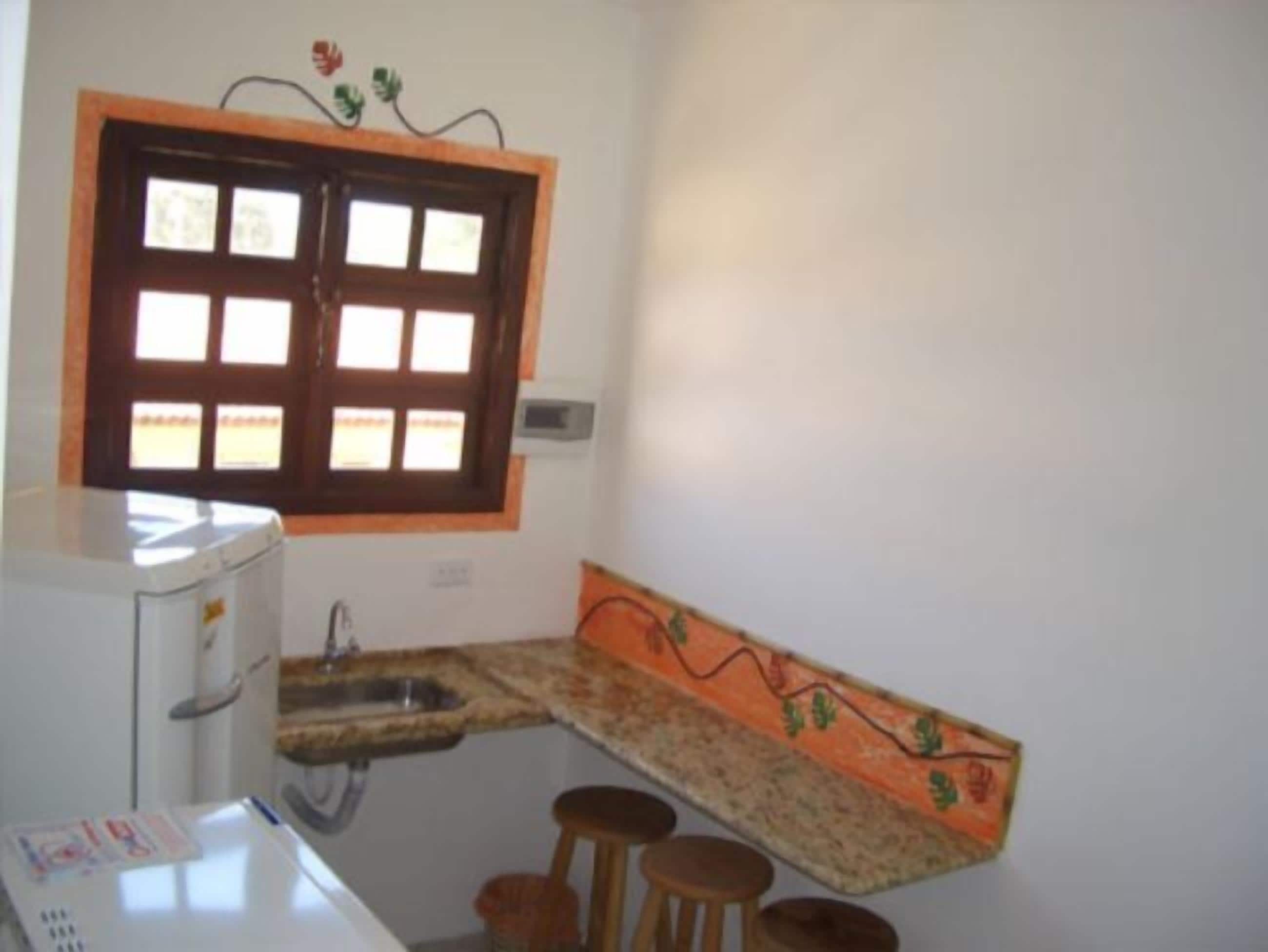 A small kitchen with a window, a sink, a countertop, and a few stools.