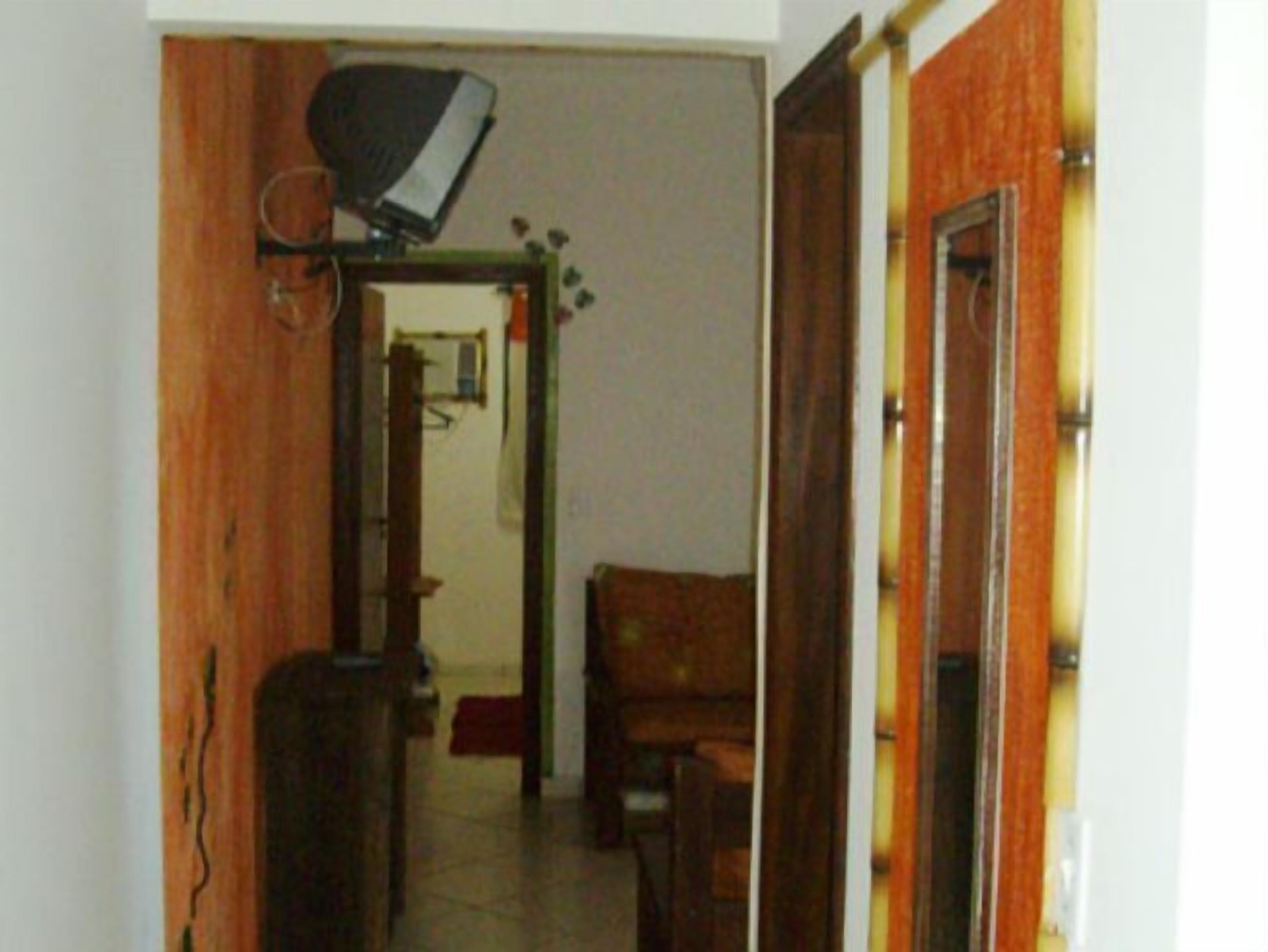 Un pasillo estrecho con una puerta de madera a la derecha, un armario de madera a la izquierda y una silla en el centro.