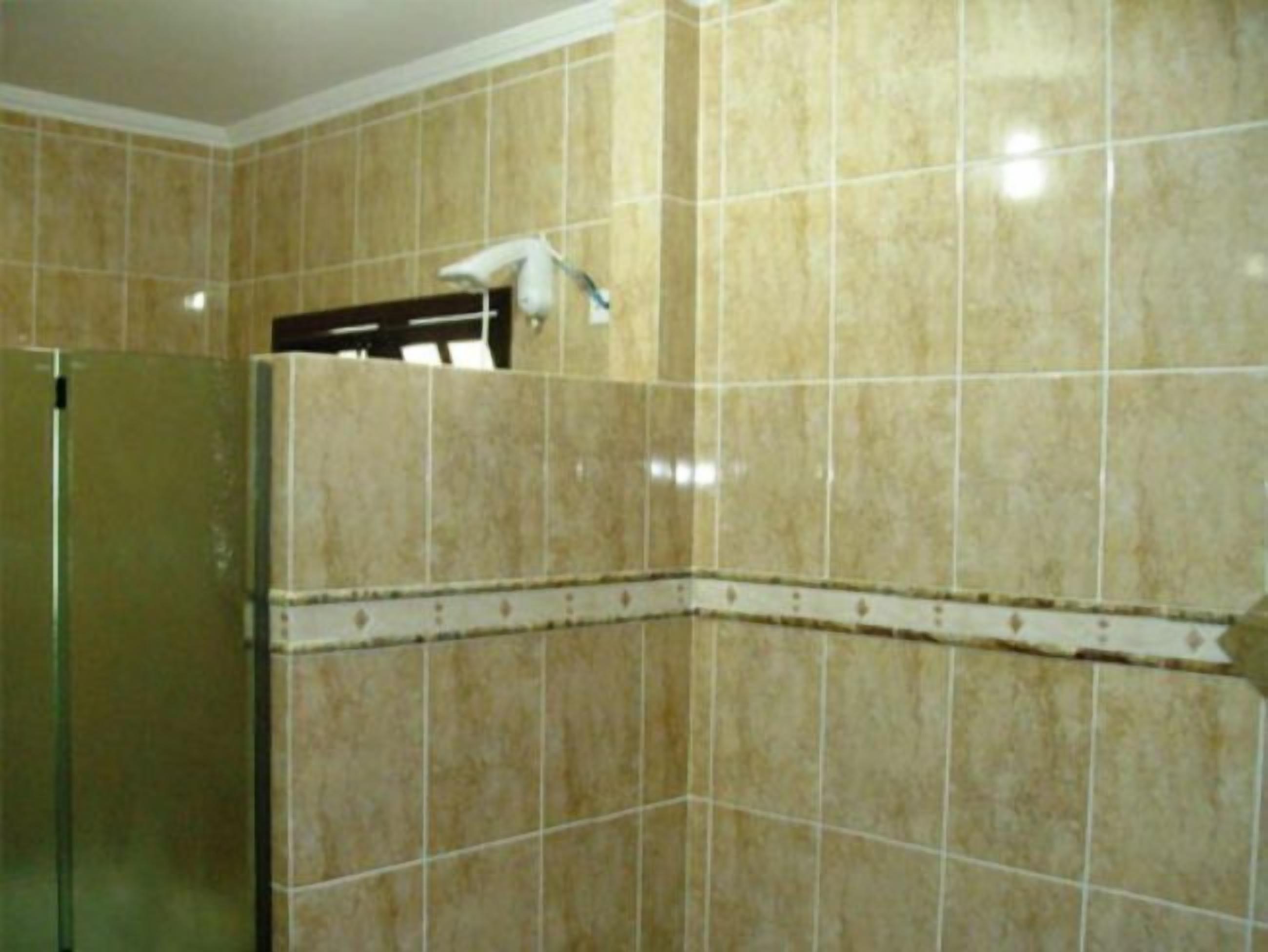 Un baño con baldosas color crema, cabina de ducha de vidrio y un picaporte visible.