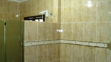 Un baño con baldosas color crema, cabina de ducha de vidrio y un picaporte visible.