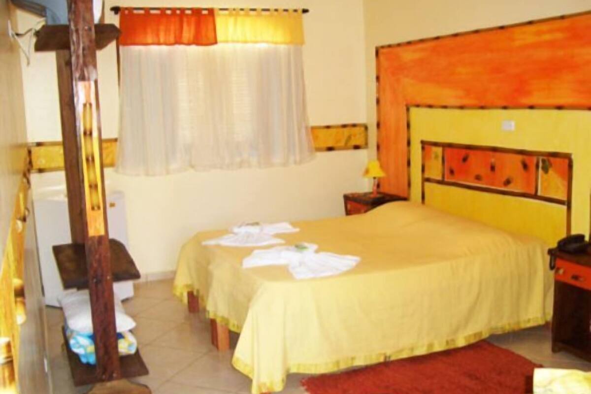 A hotel room with a bed, a nightstand, a lamp, a window with curtains, and a wooden chair.