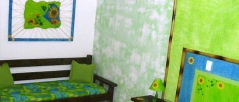 Una habitación con una cama, una mesita de noche con una lámpara y una pared con un mural verde.
