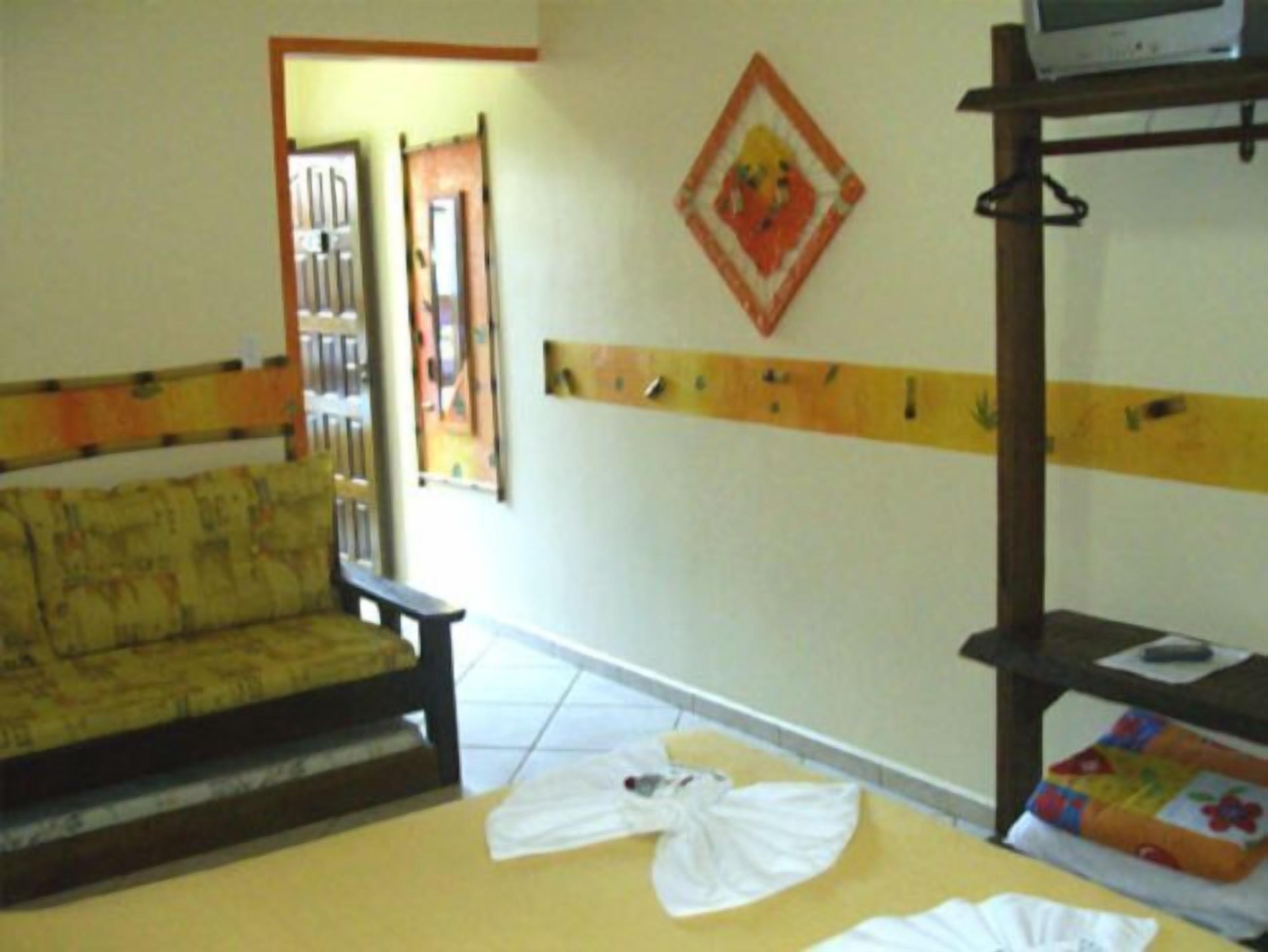 A room with a sofa, a bench, a bed with a quilt, and a television on a stand.