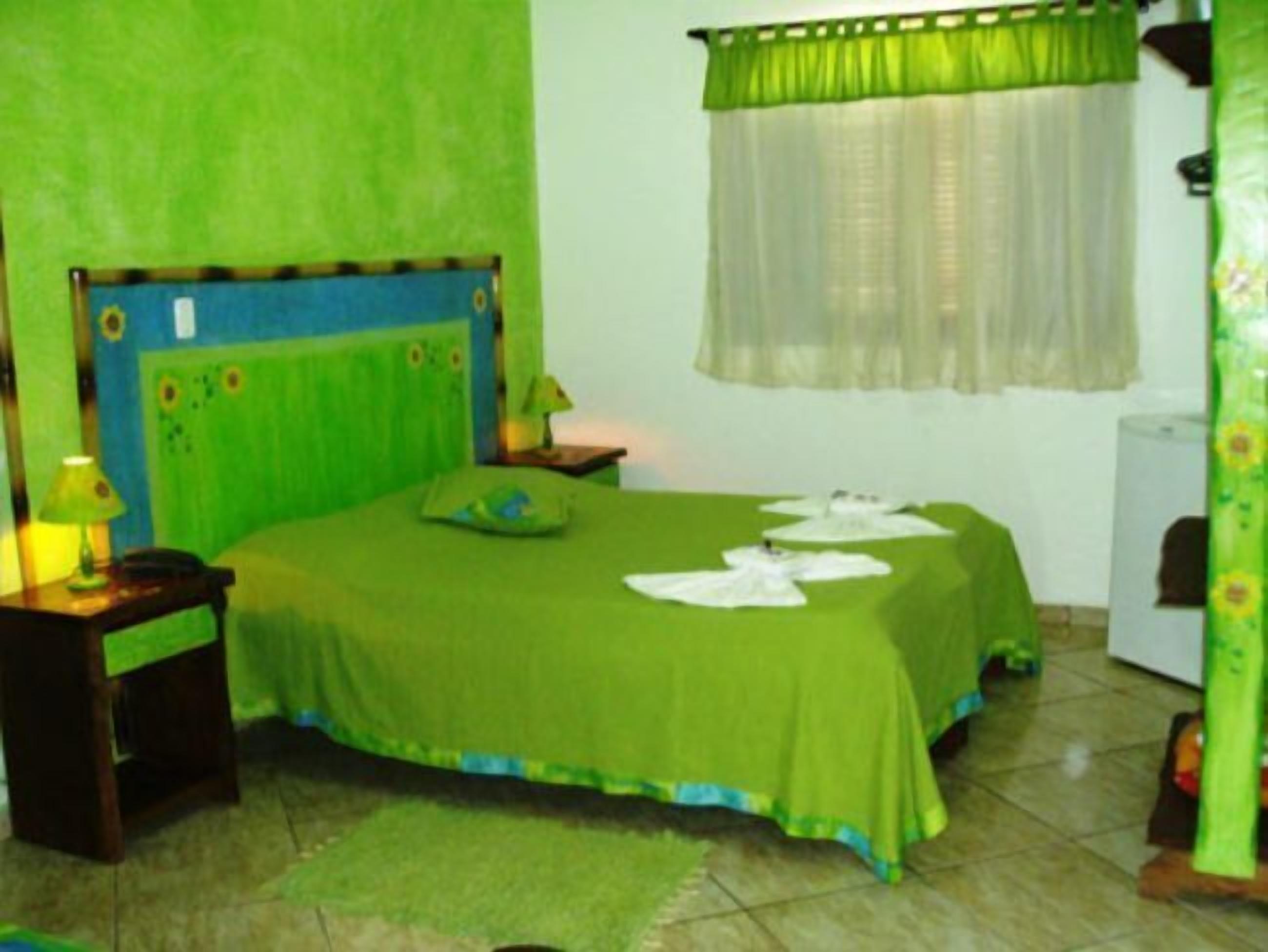 A room with a bed, a nightstand, a lamp, and a window with sheer curtains.