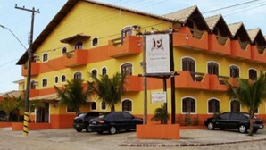 A yellow building with multiple balconies and parked cars in front. - Peruibe Suites Flat (Peruíbe)