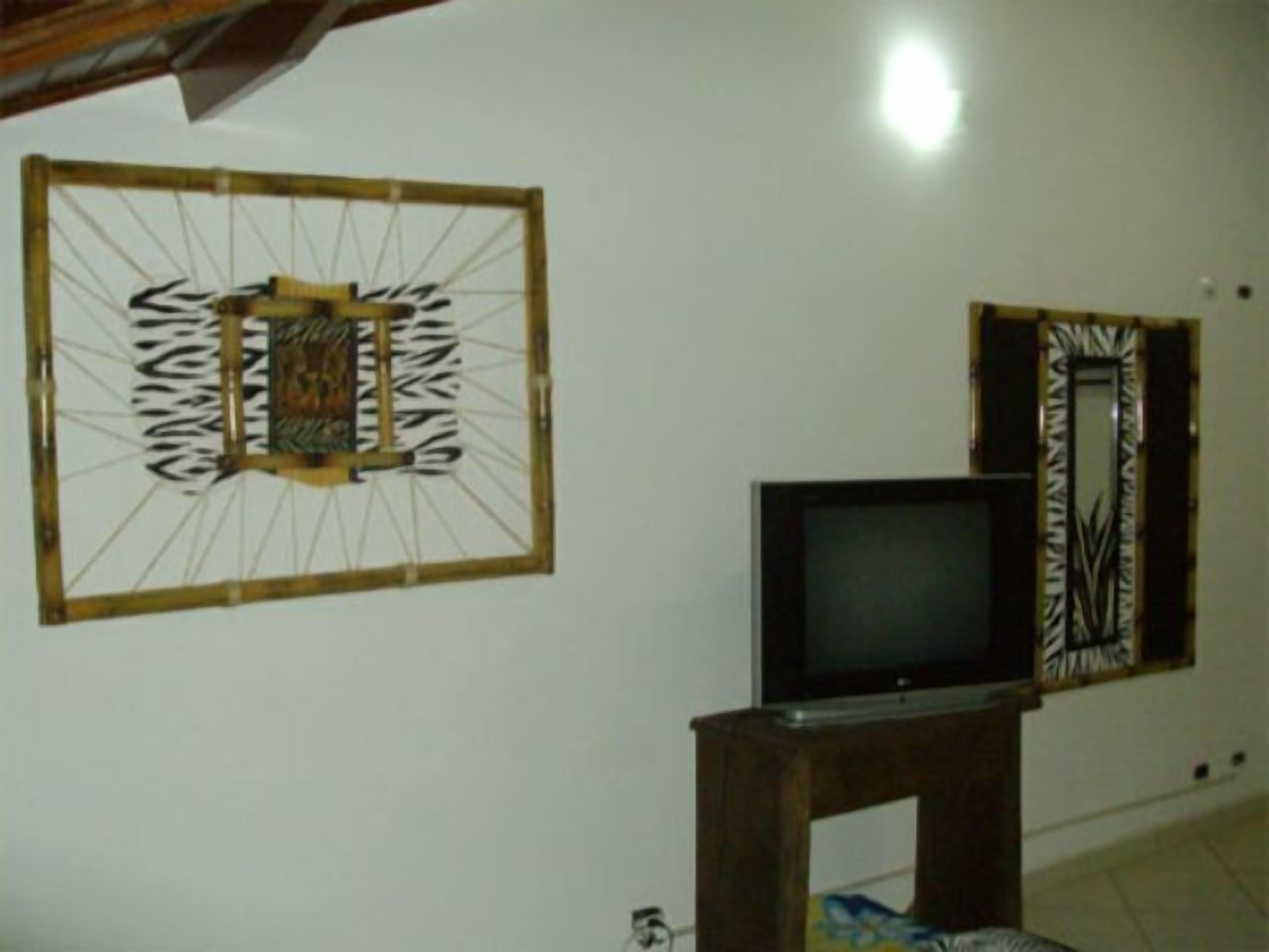 A room with a television on a wooden stand, a decorative wall piece, and a patterned door.