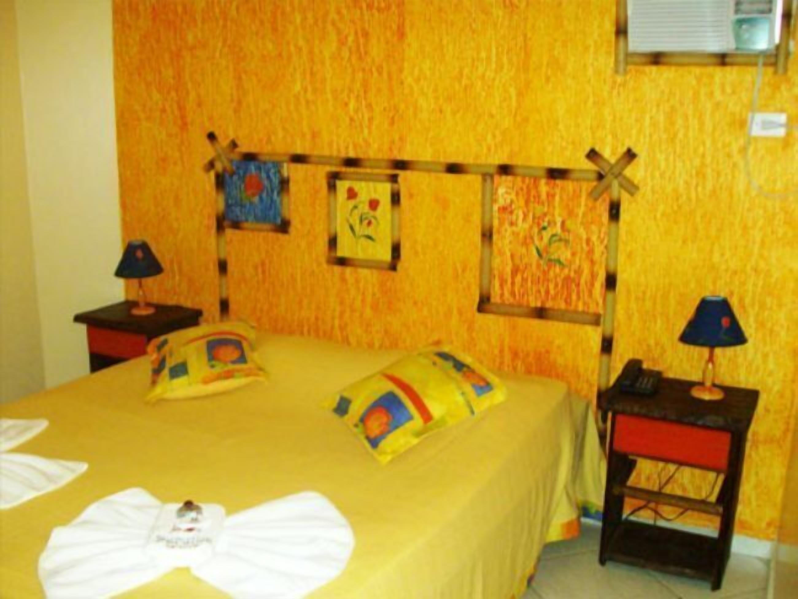 Une chambre d’hôtel comprenant un lit, deux tables de chevet, un climatiseur fixé au mur et un petit bureau avec une lampe.