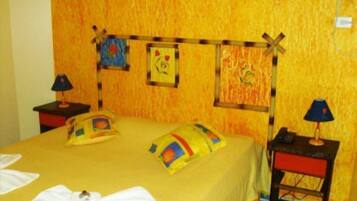 Une chambre d’hôtel comprenant un lit, deux tables de chevet, un climatiseur fixé au mur et un petit bureau avec une lampe.