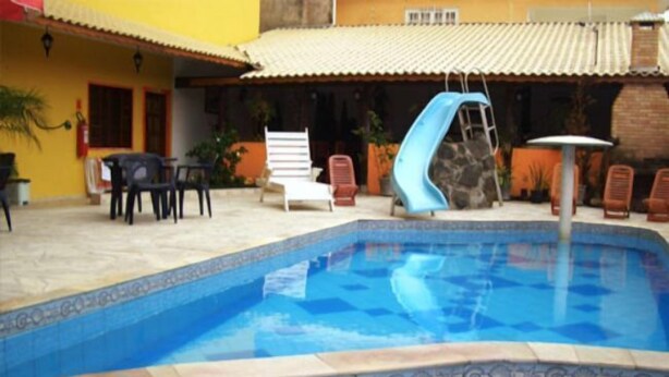 Une piscine avec un toboggan bleu, entourée de chaises longues et dotée d’une terrasse carrelée.