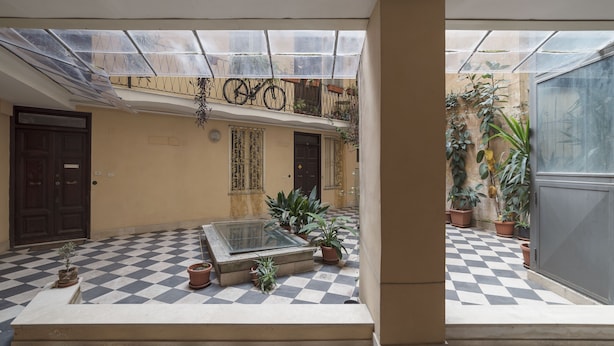 Un patio con suelo a cuadros, plantas en macetas, una mesa de vidrio y una puerta.