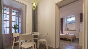 Una habitación con cama, una mesita con sillas, una planta en maceta y una ventana con cortinas.