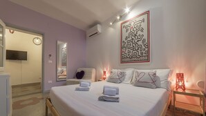 Una cama bien hecha con toallas, aire acondicionado de pared, un televisor de pantalla plana y un elemento decorativo en la pared.